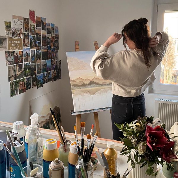 Künstlerin Noenya vor Leinwand mit Bergen und Sonnenuntergang in abstrakter Kunst