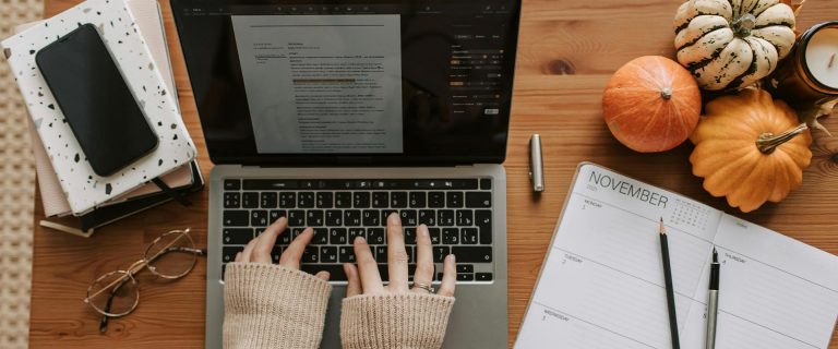 Herbst Ziele erreichen: Frauenhände am Laptop, daneben Kalender, Smartphone und Herbstdeko