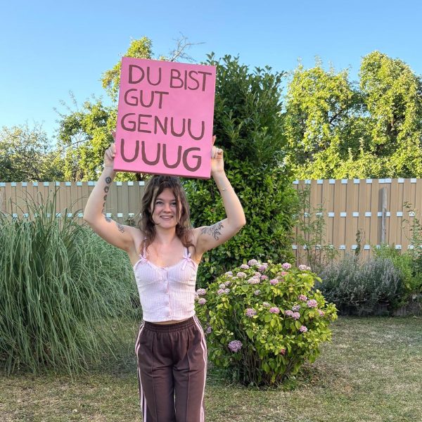 Du bist gut genug – Künstlerin Noenya hält Kunstwerk hoch, im Garten